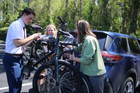 Elder Carter Snow (from left) helps Sisters Kimberlie Palmer and Tara Wallace secure their bikes on a bicycle rack on Thursday afternoon in the Church of Jesus Christ of Latter Day Saints parking lot on Old Country Club Road. The missionaries were taking part in Transfer Day where they were pairing-up with new companions to conduct their mission work. (TONY BRITT/Lake City Reporter)