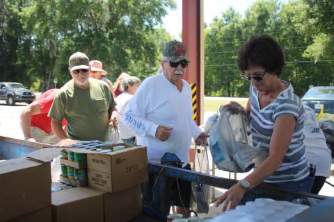 Mark Nelson (from left) and Bill Cooper wait in line as Tina Scavetta collects different canned foods while preparing food bags that will be given to local residents. Cooper, Nelson and Scavetta are volunteers supporting the North Central Florida Young Marines food distributions in Fort White. (TONY BRITT/Lake City Reporter)
