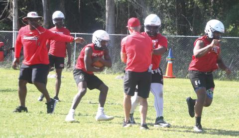 Fort White coach Demetric Jackson (left) hands the ball off to running back Maliki Clark (middle) during practice on May 1. (MORGAN MCMULLEN/Lake City Reporter)