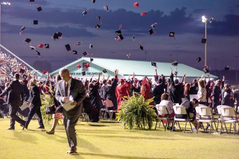 Fort White High graduates toss their caps in the air at the end of Friday’s commencement ceremony at Arrowhead Stadium as Superintendent Lex Carswell (foreground) walks off the field. (RAY CARPENTER/Special to the Reporter)