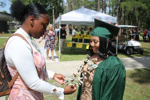 Gardine Raymond (from left) inspects the ‘money lei’ worn by her best friend Erika Maceira following Florida Gateway College’s 2023 Spring Commencement Ceremony on Friday morning. (TONY BRITT/Lake City Reporter)