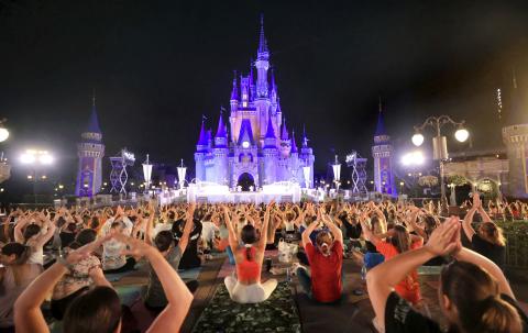 Walt Disney World cast members stretch at Cinderella Castle in a pre-dawn gathering during an annual team yoga session to commemorate International Yoga Day. (JOE BURBANK/Orlando Sentinel via AP)