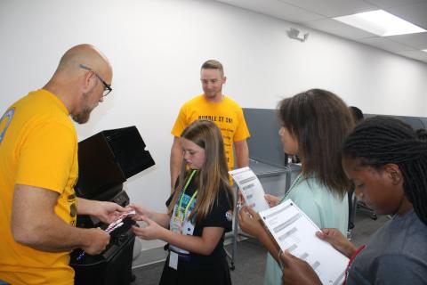Columbia County Supervisor of Elections Office employee Dennis Chauncey hands a sticker to an Eastside Elementary School fifth grader after she voted in the school’s election Tuesday. Other students wait in line with their ballots. (TONY BRITT/Lake City Reporter)