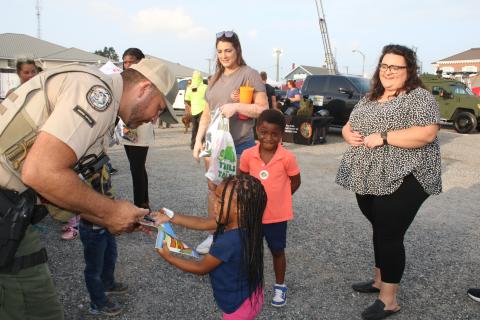Luke Davenport, a Florida Fish and Conservation Commission officer, signs a coloring book for Ava Flores, 2, as Elias Flores, 4 and Chelsea Flores (far right) look on. (TONY BRITT/Lake City Reporter)