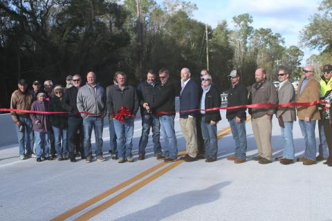 Suwannee County Commissioners Travis Land and Leo Mobley (middle) cut the ribbon Monday marking the reopening of the 180th Street bridge across Little River. (JAMIE WACHTER/Lake City Reporter)