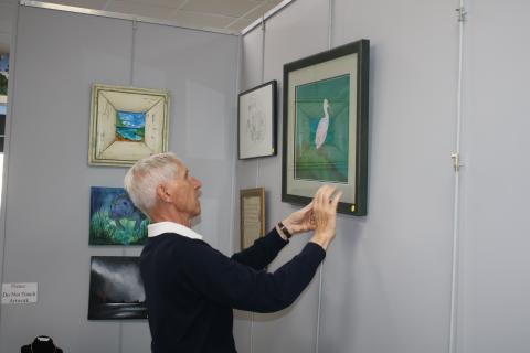 Jim Riley, former president of the Art League of North Florida and the Gateway Art Gallery, hangs up an entry into the 10th annual winter art show on Saturday. (TONY BRITT/Lake City Reporter)