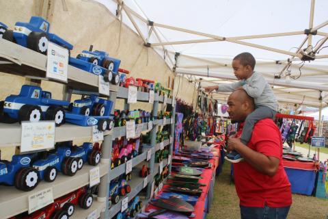 Keaven Jones gives Kaden Jones, 2, a ride on his shoulders as the youngster points out wooden cars in a vendor’s both on Friday afternoon at the 45th Annual Olustee Festival. (TONY BRITT/Lake City Reporter)