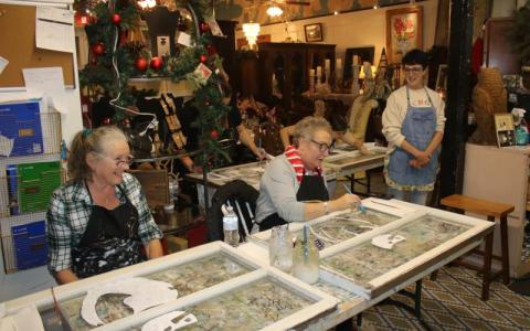 Tina Teasley (from left) and Tami Saperstein paint a snowman on window panes during an art class at the Blue Goose Studio during December’s Art Stroll. (FILE)
