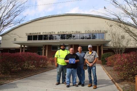Rapid Fiber Internet Vice President of System Operations Chris McKenzie holds up a ‘Free Wi-Fi’ sign in front of the Suwannee County Coliseum after EnterSource, Rapid Fiber’s installation contractor, added the service to the public facility. EnterSource staff are pictured with McKenzie. (COURTESY)