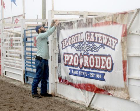 Dyllan Romanik attaches a sign in the Florida Gateway Fairgrounds rodeo arena ahead of the 30th annual Florida Gateway Pro Rodeo, which will take place Friday through Sunday. (TONY BRITT/Lake City Reporter)