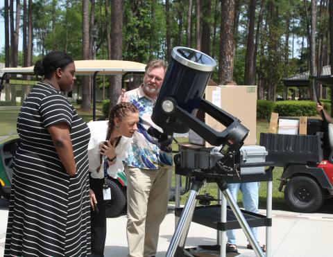 Jessica Ervienn (middle) squints as she looks through a telescope to watch Monday’s solar eclipse as she gets tips from FGC physics professor James Givviens. (TONY BRITT/Lake City Reporter)