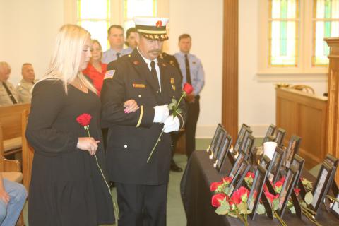 Julie Boozer, accompanied by Lt. Greg Sund, prepares to place a rose at the base of her father’s portrait during Tuesday’s Public Safety Memorial. Boozer’s father, Dwight, was Lake City’s assistant fire chief. (TONY BRITT/Lake City Reporter)