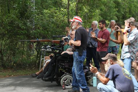 Pete Herrick, surrounded by friends and family, reacts after firing a breath-powered .308 rifle to set off a stack of cakes filled with Tannerite binary explosives Saturday during his ‘Alive Party.’ Herrick, a Fort White man, was seriously injured during Operation Iraqi Freedom 20 years ago today. (MORGAN MCMULLEN/Lake City Reporter)