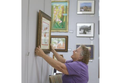 Janet Hans, an artist and a volunteer jewelry-making instructor at the Gateway Art Gallery, hangs artwork for the Gallery’s Christmas in July reception today. (TONY BRITT/Lake City Reporter)