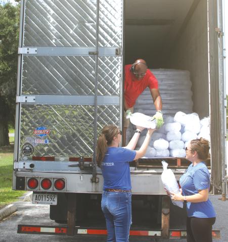 Justice Kite (from left) gets a bag of ice from Darius Parker as she and Cassie Burke, Vystar employees, prepare to give the ice to southern Columbia County residents who were left without  electricity following Hurricane Debby. (TONY BRITT/Lake City Reporter)