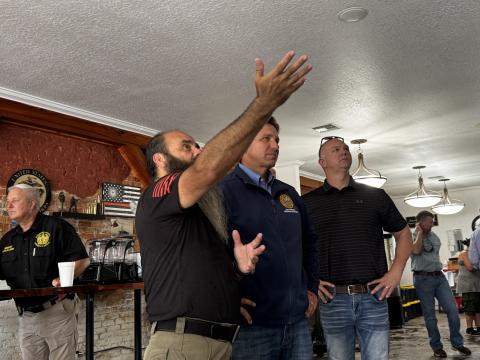 Felix Menjivar, owner of .50 Cal Coffee and Desserts, shows Gov. Ron DeSantis and Suwannee County Development Services Director Ron Meeks items on the wall of his downtown Live Oak coffee shop on Wednesday afternoon. DeSantis took a tour of downtown Live Oak to see the damage flood waters caused by Hurricane Debby. (JAMIE WACHTER/Lake City Reporter)