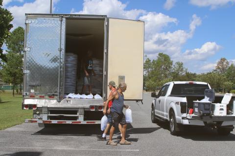 Tony Humphreys and Tony Dale, who live in a neighborhood off State Road 47, carry bags of ice from a trailer at the Southside Sports Complex to their truck on Sunday afternoon. (TONY BRITT/Lake City Reporter)