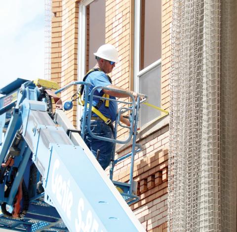 A worker measures a window on the outside of Lake City Hall on Tuesday as work begins to determine what is causing issues with the bricks on the historic building so the protective netting can be removed. (TONY BRITT/Lake City Reporter)