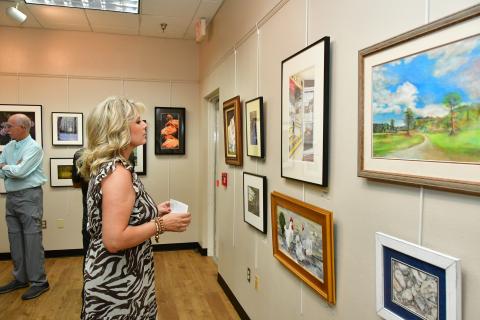 An attendee at last year’s Autum Artfest opening reception checks out some of the submitted artwork, including Chris Flanagan’s ‘City Drugs’ (top middle), which won best of show. (FILE)