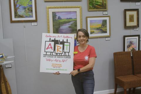 Sheila Carr, Gateway Art Gallery curator, is pictured with an Art League sign after they closed on purchasing their downtown building Thursday. (TONY BRITT/Lake City Reporter)