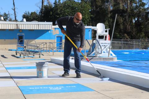 Chris Cuadras, the new aquatic director for the Columbia County School District, applies some Cool Deck paint to the concrete around the pool Monday. (JAMIE WACHTER/Lake City Reporter)