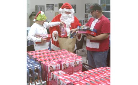 Kimberly Belcher (from left), Santa, and John Cole pack a bag with toys during the Kids Feeding Kids Grinch Christmas event on Sunday evening. (TONY BRITT/Lake City Reporter)