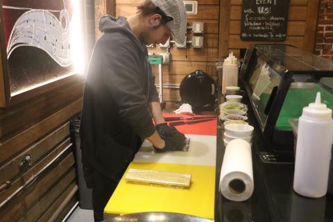 Tyler Hilton, a sushi chef at The Tavern, rolls up some sushi Friday afternoon as part of the Ribs and Rolls lunch special. Among that lunch menu is the Cowboy Roll, which is made with brisket, cream cheese, barbecue sauce and green Sriracha and then is deep fried. (MORGAN MCMULLEN/Lake City Reporter)