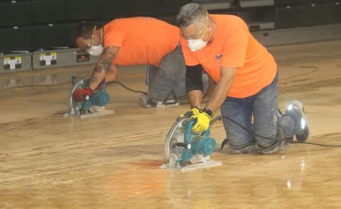 Frank Roque (foreground) and Corey Watkins of Impact Sport Surfaces Inc., use saws to cut FGC’s old parquet basketball court. (TONY BRITT/Lake City Reporter)