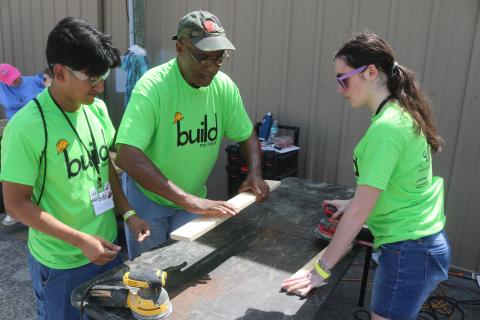 Angel Gomez, a Columbia High School student, gets tips on sanding wood from Monty Ashby, as Gomez and Kiley Morrison sand wood to make beds for the Sleep in Heavenly Peace program. The students manufactured the beds during the Build My Future event on Wednesday morning at the Florida Gateway Fairgrounds. (TONY BRITT/Lake City Reporter)