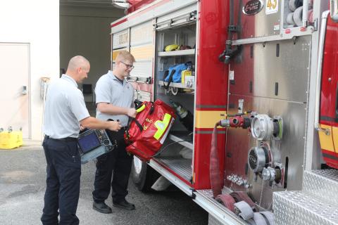 Columbia County Fire Rescue employee Jake Doyle (left) holds a cardiac monitor as Justin Ingle loads an Advanced Life Saving bag onto a fire engine at Station 43 on Friday morning. (TONY BRITT/Lake City Reporter)