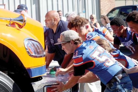 Sen. Corey Simon (left) is joined by seniors on the Branford football team Tuesday morning in pushing in the Branford Volunteer Fire Department’s new engine, which was obtained with state funding. The truck is painted orange and blue to match the colors of Branford High School. (JAMIE WACHTER/Lake City Reporter)
