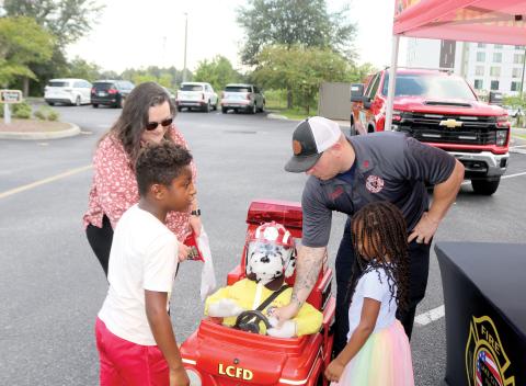 Elias Flores (clockwise from left), 6, Chelsea Flores, Lake City Firefighter Dustin Alford and Ava Flores, 4, play with Patches, a fire department remote controlled vehicle during the Fire Rescue N’ Cones event on Monday. (TONY BRITT/Lake City Reporter)