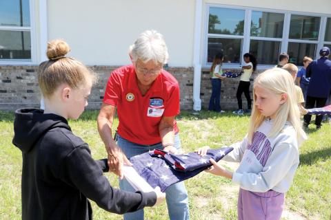 Elaine Lagasse, a member of the American Legion Post 57 Honor guard, helps a pair of Fort White Elementary School students fold a flag during a flag etiquette lesson Wednesday. (TONY BRITT/Lake City Reporter)