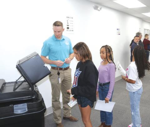 Kent Banner (left), Columbia County Assistant Supervisor of Elections, helps fifth-grade Eastside Elementary School students place their ballots into the tabulator on Tuesday morning during a school election at the county election’s office. (TONY BRITT)