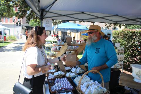 A shopper at a previous market event in downtown Olustee Park buys soap from the Kinghorn Farms booth. The City of Lake City’s Growers and Makers Market returns downtown Saturday. (FILE)