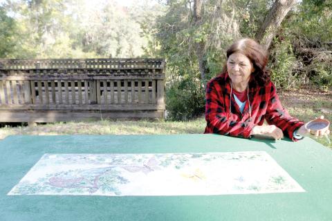 Local artist Judith McClure looks over a piece she created on a picnic table in Way Side Park in White Springs. The Our Community Cares Coalition, adults, youth members and community volunteers are creating a mural at the park’s boat ramp to go along with adding images to picnic tables at the park. (TONY BRITT/Lake City Reporter)