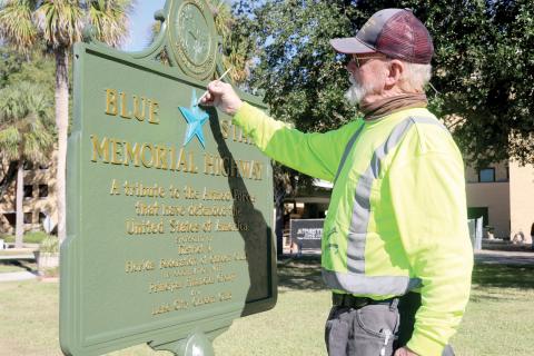 Thomas L. Stelling with Historical Markers Restorations paints the blue star on the Blue Star Memorial Highway marker that sits in front of the Lake City VA Hospital. Stelling restored the sign last week for the Lake City Garden Club. (TONY BRITT/Lake City Reporter)