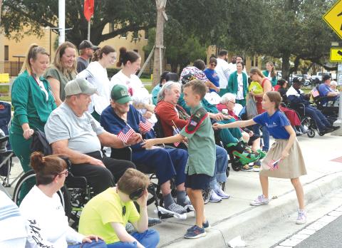 A pair of youngsters hand out American flags to veterans and others during Saturday’s Veterans Day parade in Lake City. (TONY BRITT/Lake City Reporter)