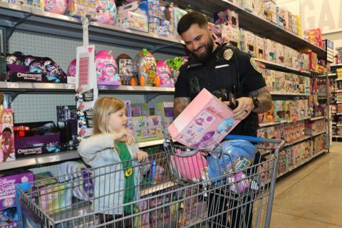 Kylin Barwick, 7, gets a smile from Lake City police officer Kevin Johnson as she tells him about a toy she plans to purchase during the Shop With A Cop event on Wednesday morning at Walmart. (TONY BRITT/Lake City Reporter)