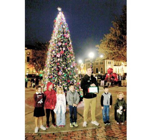 Lake City Mayor Noah Walker is helped by Sierra Lacy (from left), Ariah Leonard, Willow Leonard, Liam Villamil and Legend Brown in lighting the Christmas tree in downtown Olustee Park on Monday night. (TONY BRITT/Lake City Reporter)