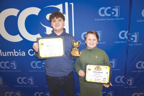 Fort White Middle School student Tucker Ayers (left) holds his certificate and trophy alongside his younger brother, Benjamin Ayers, after winning the 2026 Columbia County Schools First Coast Spelling Bee Friday. (COURTESY)