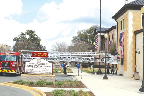 Lake City Fire Department firefighters use their Tower 1 truck to hang the American Flag on the Columbia County Commission Annex Building on Saturday morning. (TONY BRITT/Lake City Reporter)