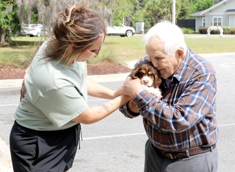 Stephanie Spradley with Spradley Springers passes a puppy to Donald Altman to love on during activities at the Easter Extravaganza at the Canopy at Harper Lake on Saturday. (TONY BRITT/Lake City Reporter)