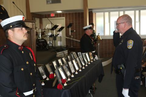 Lake City police officer Greg Burnsed salutes pictures of fallen first responders after placing a flower in honor of them at last year’s Public Safety Memorial. (FILE)