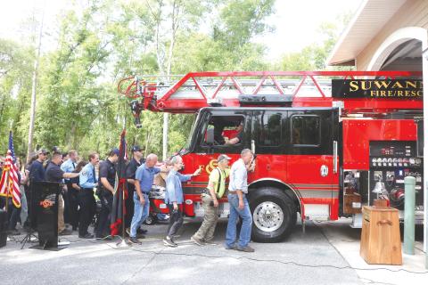 Suwannee County Commissioner Travis Land leads a group of county residents and firefighters in pushing the new ladder truck into the Dowling Park station Wednesday morning. (MORGAN MCMULLEN/Lake City Reporter)