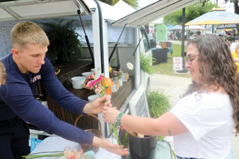 Kaiden Flint (from left) helps Jaime Greenwood as she makes a purchase from the Early Bird Flower Truck during the Spring Market and Multi-Cultural Day event. (TONY BRITT/Lake City Reporter)