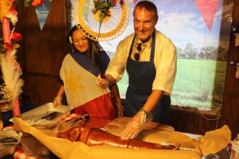 Mayla Beaty (left), the incoming president of Filipino-American Cultural Society of Lake City, stands with the Peter Howell as he prepares to cut the roasted pig during the Philippine Independence Day celebration at Quail Heights Country Club on Saturday. (TONY BRITT/Lake City Reporter)