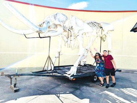 A couple of people pose under the replica mastadon skeleton that was on display at the Columbia County Public Library during a summer kickoff event on Friday. (COURTESY)