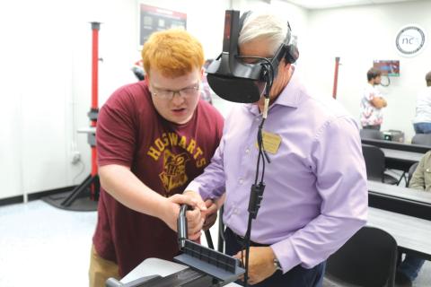 Brody Hoffman (left), a Florida Gateway College student, helps Mitchell Maione, a coordinator for the FGC physical therapy program, as Maione uses a VR welding simulator during the college’s grand opening for its newly renovated welding technology program on Tuesday afternoon. (TONY BRITT/Lake City Reporter)