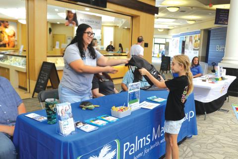 Vivian Jones (from left) of Palms Medical Group gives a book bag to Erin Neal, 10, at the Lake City Mall on Saturday during the Movin’ and Groovin’ Back to School event. (TONY BRITT/Lake City Reporter)